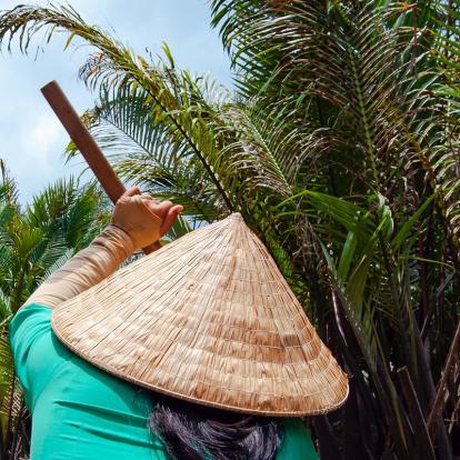 Woman wearing conical straw hat cruises in the Mekong Delta jungle