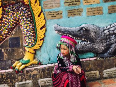Girl in traditional dress sat in front of street art mural in Chiang Mai